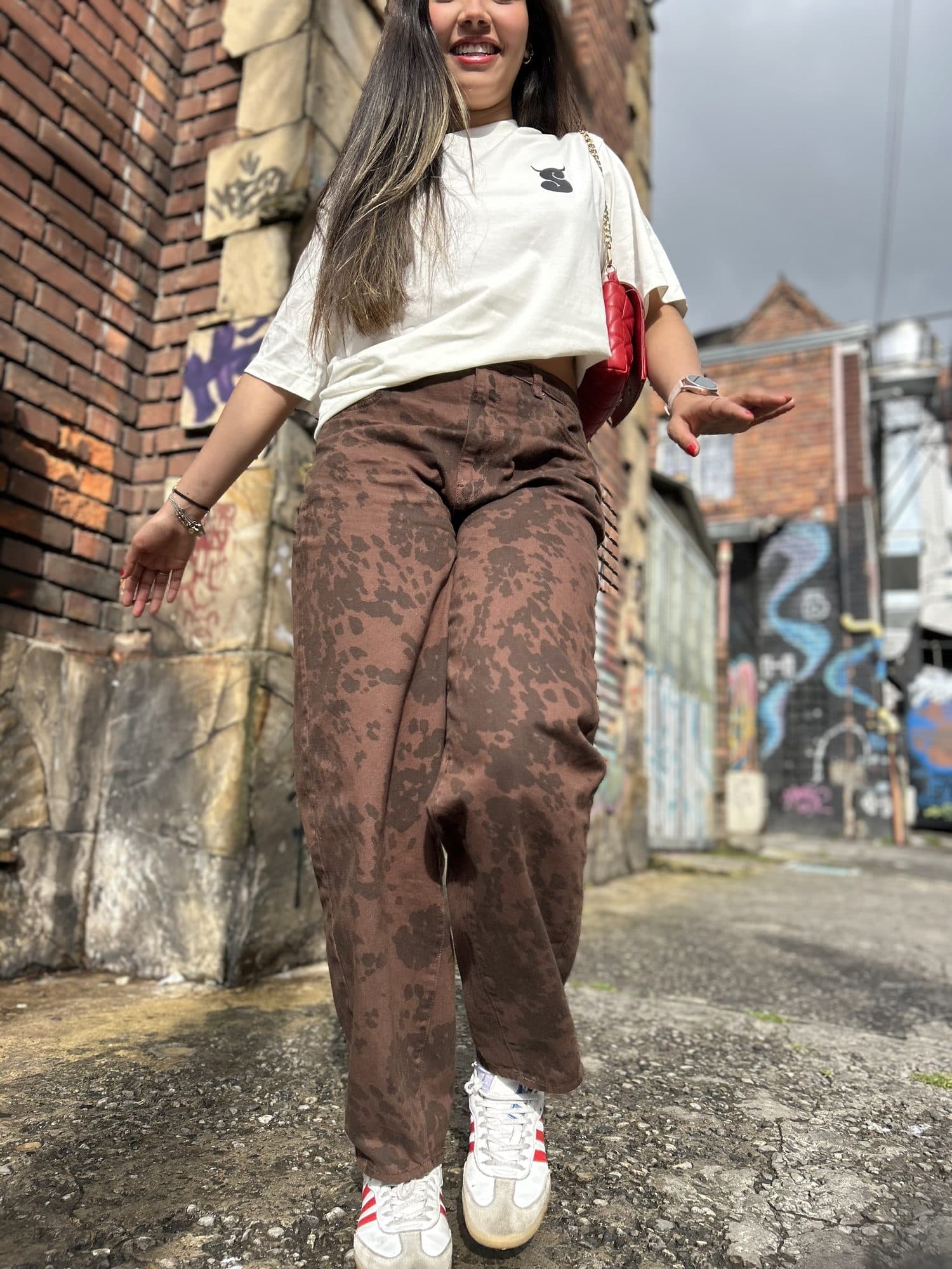 Modelo con la camiseta Intrinsic blanca y pantalón café en una calle con grafiti