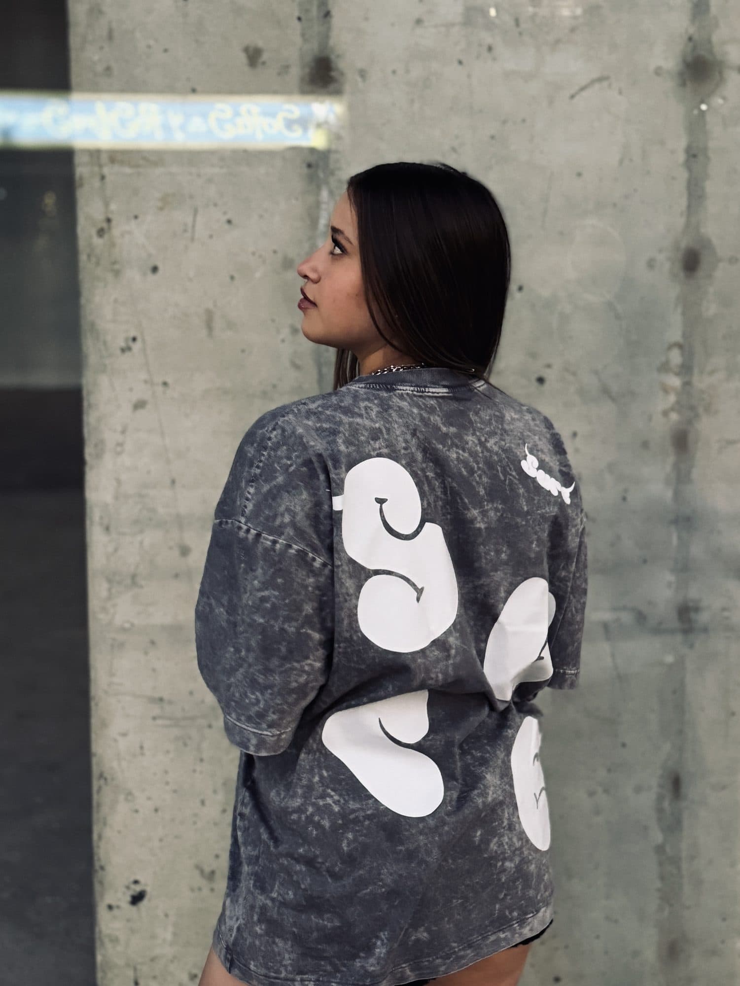 Modelo de espaldas contra una pared de concreto con la camiseta Niebla