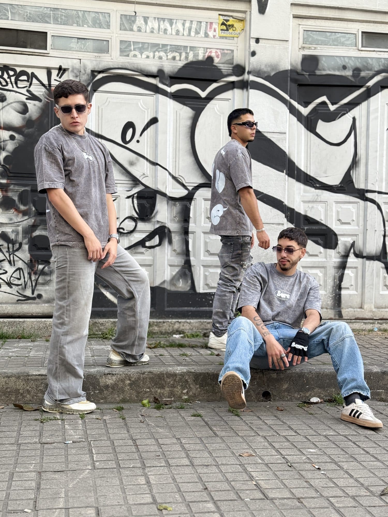 Tres personas con camisetas Niebla frente a una puerta con grafiti