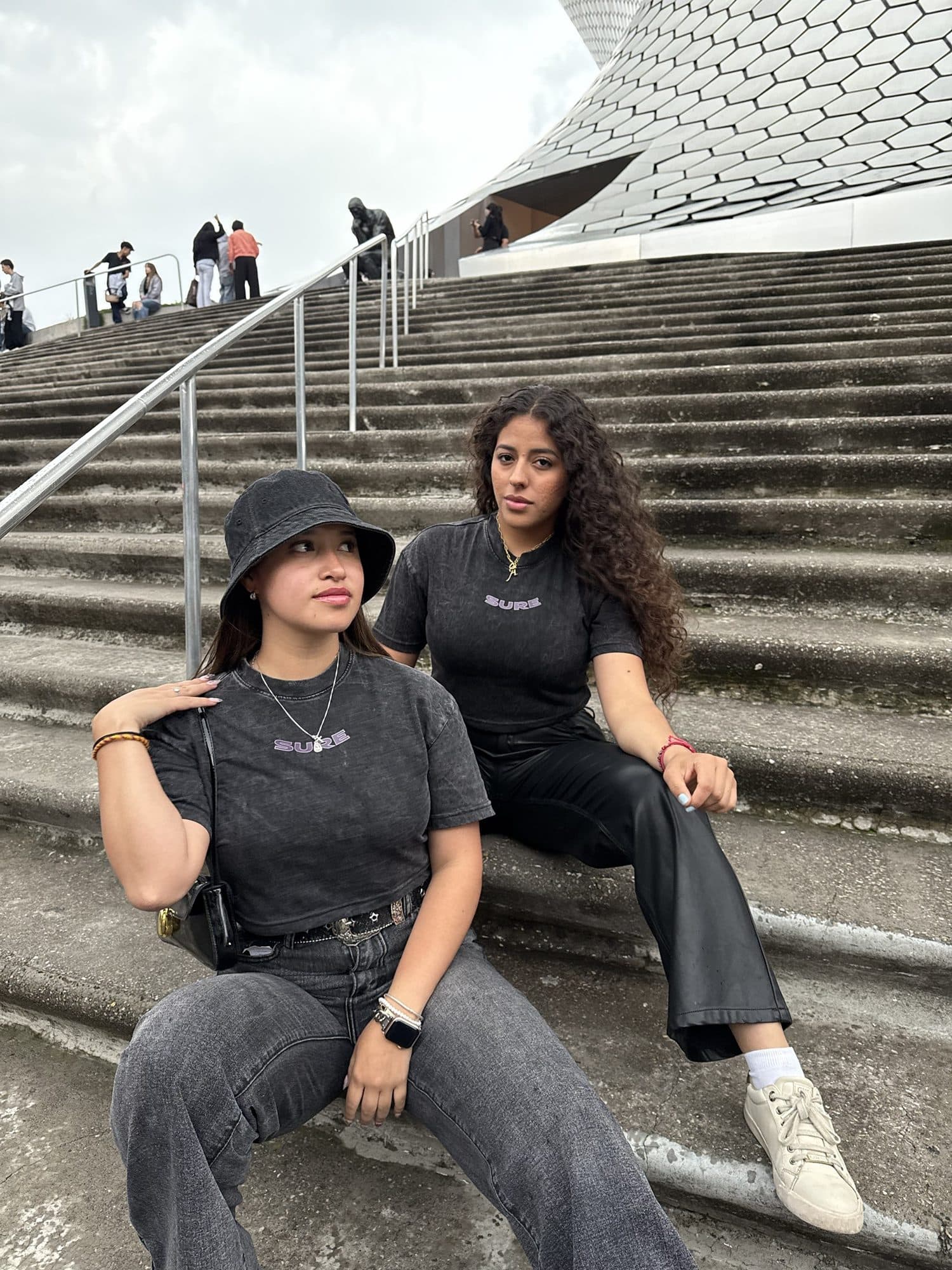 Dos modelos sentadas en una escalinata con los crops gris carbón y SURE en morado