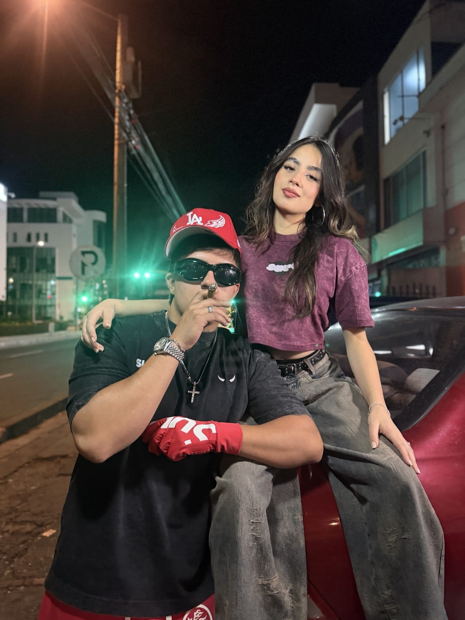 Pareja de noche junto a un carro rojo con la camiseta gris carbón y el crop vino tinto