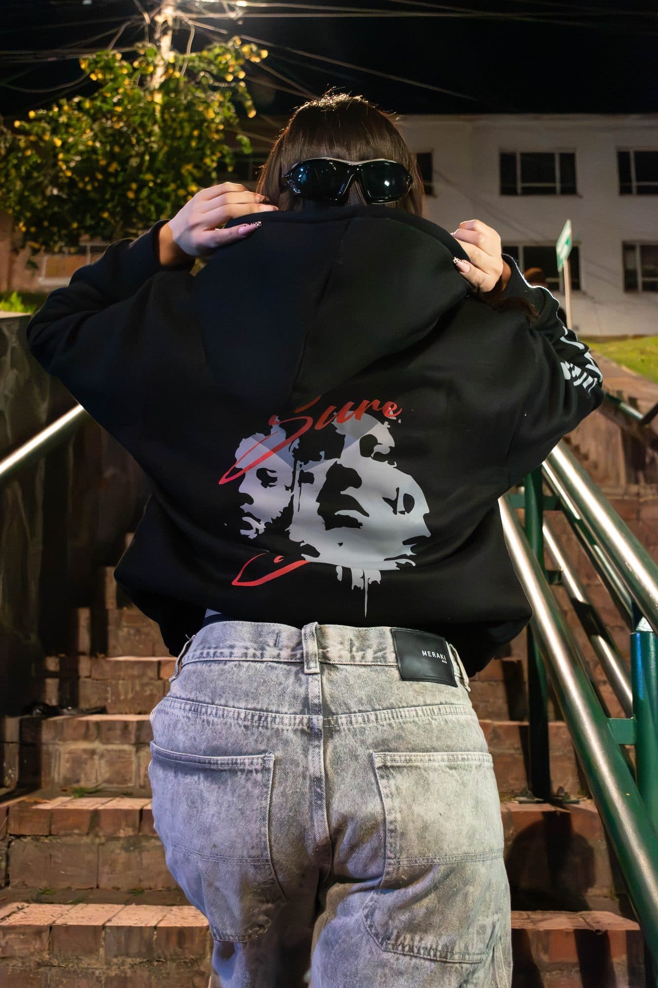 Modelo de espaldas subiéndose la capucha del hoodie Disidencia en una escalera