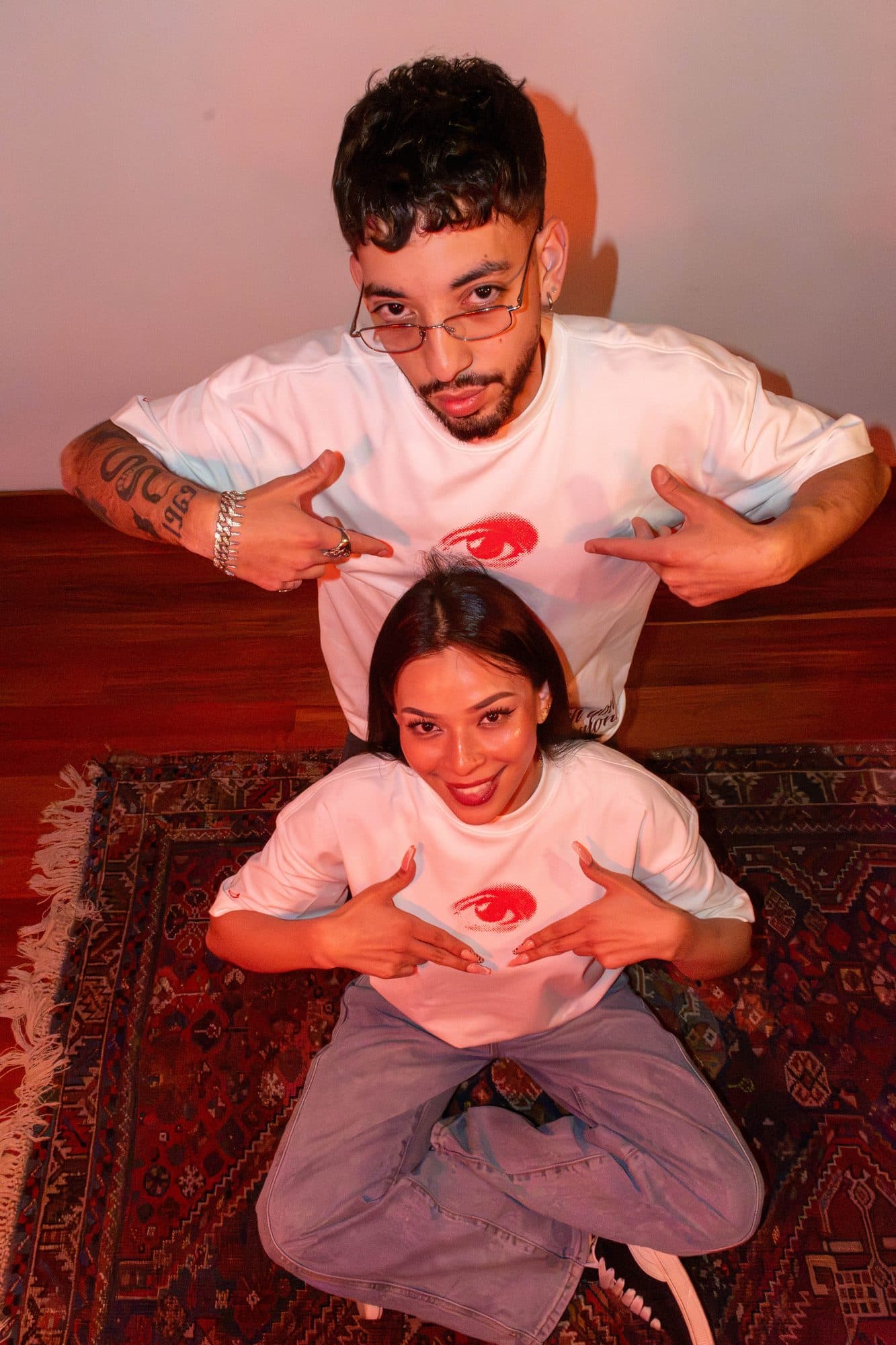 Dos modelos sobre una alfombra señalando el ojo rojo de la camiseta Disidencia