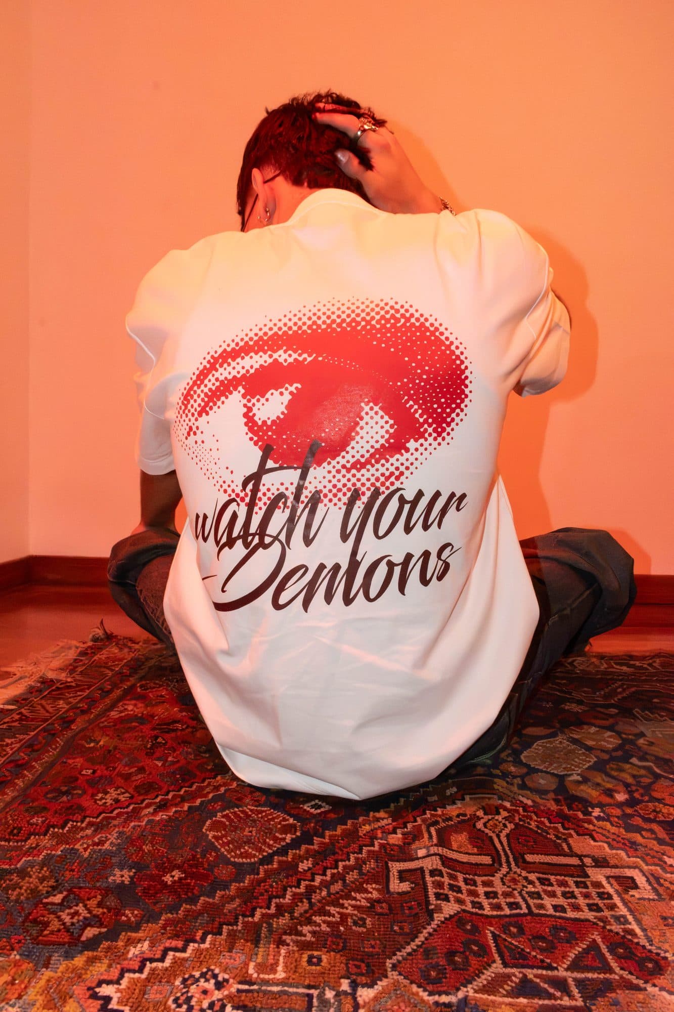Modelo sentado de espaldas mostrando el ojo y Watch Your Demons