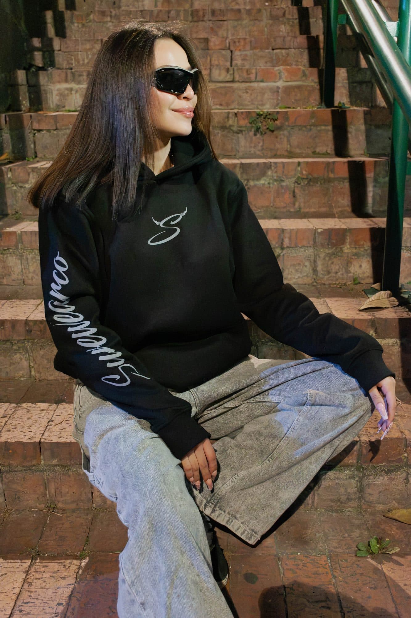 Modelo sentada en una escalera con el hoodie Disidencia; se ve Surewearco en la manga